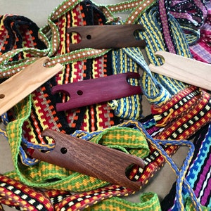 May include: A close-up of five wooden weaving tools, each with a different color and grain. The tools are surrounded by colorful woven bands.