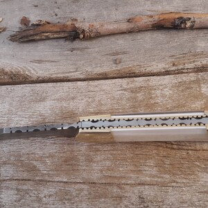 May include: A closed pocket knife with a silver blade and a brass handle. The blade has a decorative pattern of small circles. The handle has a decorative pattern of small circles and a brass pin.