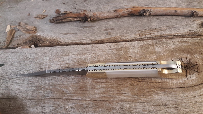 May include: A closed pocket knife with a silver blade and a brass handle. The blade has a decorative pattern of small circles. The handle has a decorative pattern of small circles and a brass pin.