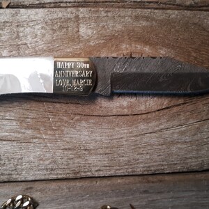 May include: A pocket knife with a white handle and a black blade. The knife has a gold inscription that reads "HAPPY 30th ANNIVERSARY LOVE MARCIE 10-12-93".