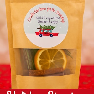 Może przedstawiać: Brązowa papierowa torba z przezroczystym okienkiem, zawierająca laskę cynamonu, plaster pomarańczy i zieleń. Okrągła naklejka głosi "Smells like home for the Holidays" z instrukcjami i czerwonym samochodem przewożącym choinkę.