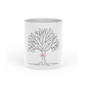 Op de afbeelding: Witte keramische mok met een zwarte lijntekening van een boom. De boom heeft bladeren en wortels, en een rood hart met de letters "A&J" in het midden. De mok is cilindrisch en heeft een glanzende afwerking.