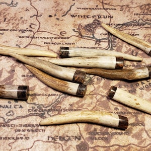 May include: A collection of eight antler tips with brown and black resin accents. The antler tips are various sizes and shapes. The antler tips are arranged on a brown background.