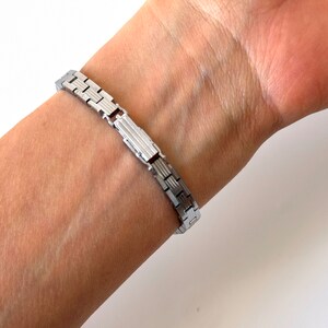 May include: A silver watch strap with a clasp fastening. The strap is made of metal links.