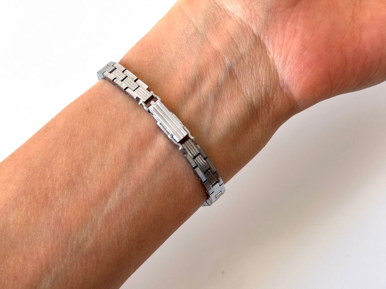 May include: A silver watch strap with a clasp fastening. The strap is made of metal links.