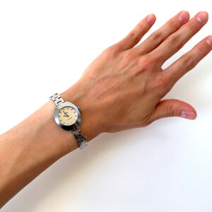 May include: A silver wristwatch with a round, white face and silver hands. The watch is on a silver metal band.