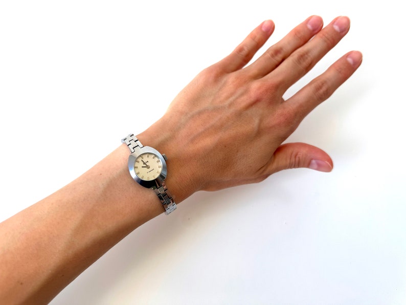 May include: A silver wristwatch with a round, white face and silver hands. The watch is on a silver metal band.