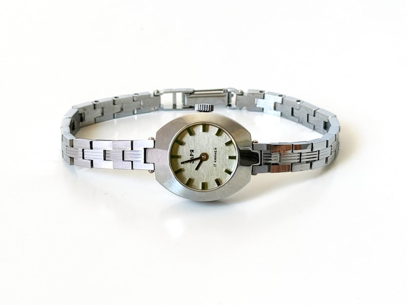 May include: A silver wristwatch with a white face and black hands. The watch has a silver metal band and says "Super" on the face.