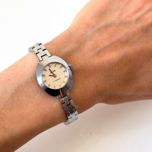 May include: A silver wristwatch with a round, slightly oval-shaped face. The watch face has a white background with black markings and the text "17 Jewels" and "C. KAMERER". The watch has a silver metal band.