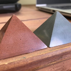May include: Two small pyramids, one brown and one grey, are sitting on a wooden surface.