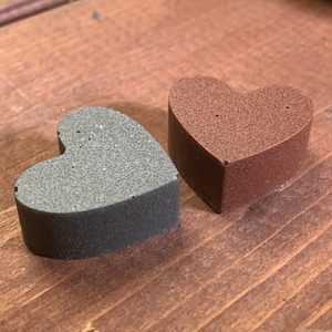 May include: Two heart-shaped foam sponges, one brown and one grey. The sponges are textured and have a slightly rough surface.