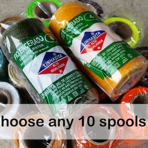 Puede incluir: Surtido de 10 carretes de hilo encerado en varios colores, incluyendo verde, amarillo, naranja, blanco y negro. Cada carrete está etiquetado con "Linhasita" y presenta el texto "Fio Encerado 100% Polyester Peso Lio 100 gramas" y "Alta Qualidade".