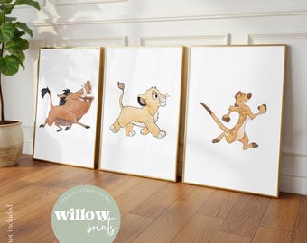 May include: Set of three framed art prints featuring watercolor illustrations of characters from The Lion King. The prints include Pumbaa, Simba, and Timon, with gold frames and white matting. The prints are displayed on a wooden floor.