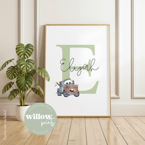 Può includere: Una stampa incorniciata con il nome "Elijah" in corsivo, con una grande lettera "E" verde come sfondo. Un camioncino dei cartoni animati è sotto il nome. La stampa è in una cornice dorata, con il testo "willow prints by Lauren" in un cerchio in basso.