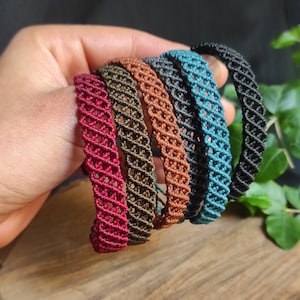 Peut inclure: Cinq bracelets tressés de différentes couleurs, dont le rouge, le marron, le vert foncé, le noir et le bleu. Les bracelets sont empilés les uns sur les autres et sont faits avec un motif tissé.