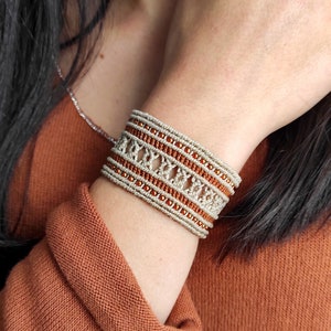 May include: A beige and brown woven bracelet with small orange beads. The bracelet is made with a macrame technique and has a geometric pattern.