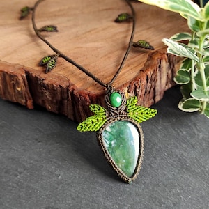 Op de afbeelding: Een hanger van groene agaat met een ketting van geknoopt koord. De hanger is omgeven door groene bladeren van geknoopt koord.