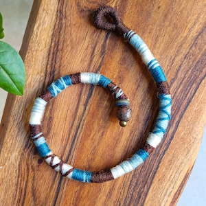 Puede incluir: Envoltura de rastas hecha a mano en tonos marrón, azul y blanco. La envoltura está hecha de hilo y presenta un acento de cuentas de madera. La envoltura está diseñada para envolverse alrededor de una rasta. El diámetro es de aproximadamente 2,5 cm.