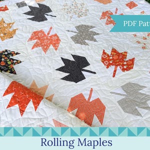 May include: A white quilt featuring a repeating pattern of maple leaf shapes in various fabrics, including orange, black, grey, and floral prints. The quilt has intricate curved quilting stitches throughout and a teal banner with the text PDF Pattern.