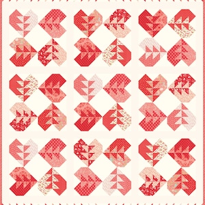 May include: A quilt with a white background and a pattern of red hearts made up of smaller red, pink, and white fabric squares. The hearts are arranged in a grid pattern and are bordered by a red and white trim.