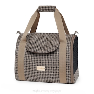 Puede incluir: Un transport&iacute;n para mascotas de color marr&oacute;n y beige con estampado de pata de gallo, con asa superior y ventana de malla. El transport&iacute;n tiene un peque&ntilde;o bolsillo en la parte delantera con un parche de cuero marr&oacute;n que dice "Muffin & Berry".