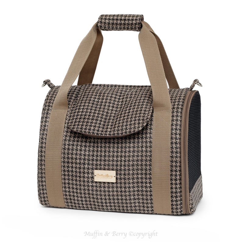 Puede incluir: Un transport&iacute;n para mascotas de color marr&oacute;n y beige con estampado de pata de gallo, con asa superior y ventana de malla. El transport&iacute;n tiene un peque&ntilde;o bolsillo en la parte delantera con un parche de cuero marr&oacute;n que dice "Muffin & Berry".