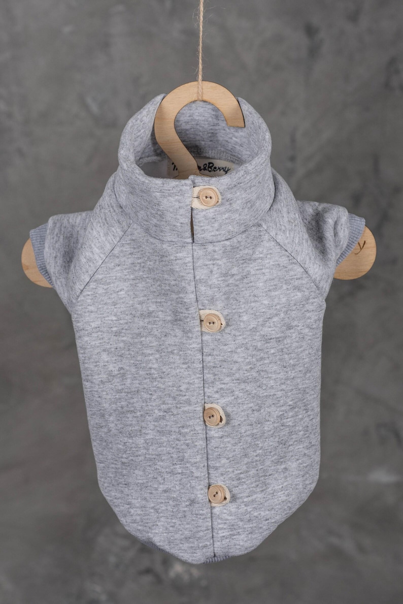 May include: A heather gray pet sweater with a high collar and four light-colored wooden buttons down the front. The garment features short sleeves with ribbed cuffs and a small interior label that reads "Twig & Berry" at the neckline.
