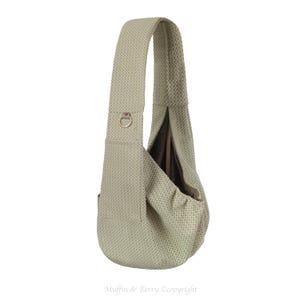 May include: A light green, textured sling bag with a single shoulder strap. The bag has a rounded shape with a deep pocket and a metal ring detail on the strap. The bag is designed to be worn over the shoulder.