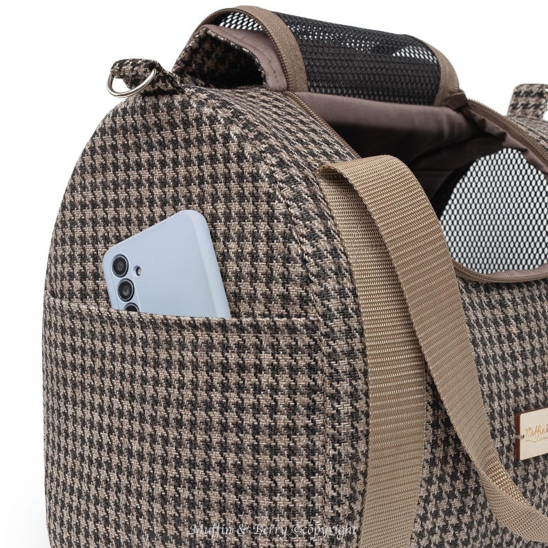 Puede incluir: Un transport&iacute;n para mascotas de color marr&oacute;n y negro con estampado de pata de gallo, con parte superior de malla y un bolsillo con cremallera en el lateral. El transport&iacute;n tiene una correa de hombro ajustable marr&oacute;n y un asa en la parte superior.
