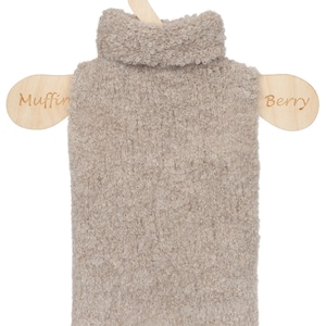 May include: A beige, textured, fuzzy turtleneck sweater displayed on a light-colored wooden hanger. The hanger features the word Muffin on the left side and Berry on the right side. The sweater has a high, folded collar and a soft, fleece-like appearance.
