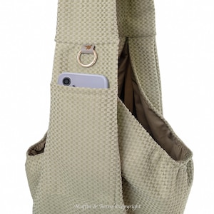 May include: A light green textured fabric sling bag with a pocket holding a smartphone. The bag has a gold-coloured ring and a small leather accent. The interior lining is a darker shade of green.