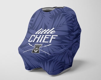 Op de afbeelding: Een marineblauwe baby autostoel hoes met een tropisch bladeren patroon. De hoes heeft de tekst "little CHIEF" in het wit, samen met een afbeelding van een tribaal ontwerp. Het ontwerp is geschikt voor een baby.