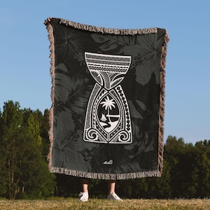 Könnte beinhalten: Eine schwarze und weiße gewebte Wolldecke mit einem polynesischen Design, das einen Palmenbaum und ein Boot zeigt. Die Decke hat einen Fransenrand und wird von einer Person gehalten.