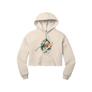 May include: A cropped hoodie in a light beige colour with a vintage-style graphic of the coat of arms of Samoa. The graphic features a palm tree, a boat, and a sunset.