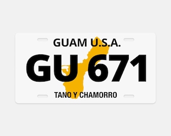 May include: White license plate with the text "GUAM U.S.A." above the bold black letters "GU 671". A yellow outline of Guam is in the center. The text "TANO Y CHAMORRO" is below.