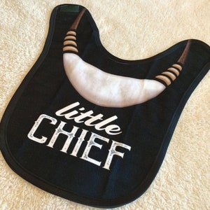 Könnte beinhalten: Schwarzer Lätzchen mit einem weißen Design in Form einer Kurve und dem Text "little CHIEF" in Weiß mit glitzernder Oberfläche.