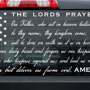 May include: A black truck with a white vinyl decal on the rear window. The decal features a stylized American flag with stars and the text "THE LORDS PRAYER" and the Lord's Prayer in cursive writing.