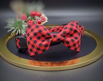 May include: Red and black plaid bow tie on a black collar. The bow tie is made of a soft fabric and has a classic bow tie shape.