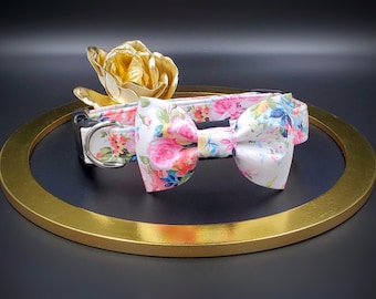 May include: A white dog collar with a floral print and a matching white bow tie. The collar has a silver buckle and the bow tie has a floral print.