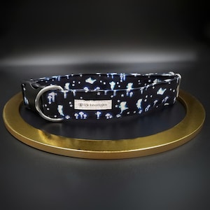 May include: Black dog collar with a whimsical pattern of white ghosts, stars, and mushrooms. The collar has a black plastic buckle and a silver metal D-ring. A small white tag with text is sewn on the collar.