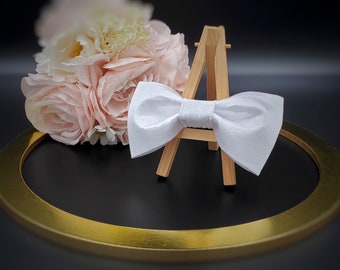 May include: A white satin bow tie displayed on a wooden easel, resting on a gold circular tray.