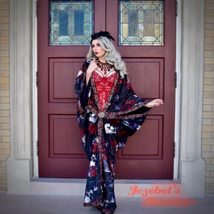 May include: A red lace bodysuit is worn under a black and red floral patterned kimono with skull accents. The kimono is cinched at the waist with a decorative clasp. The image is set against a burgundy door.