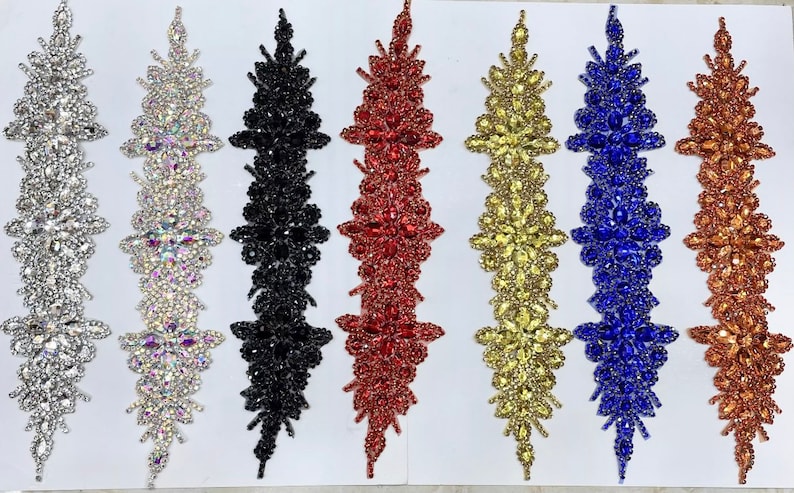 May include: Seven rows of decorative trim with various colored rhinestones. The trim is arranged in a vertical line with each row featuring a different color: clear, silver, black, red, gold, blue, and copper.