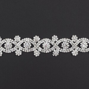 Może przedstawiać: Srebrna lamówka z kryształków z powtarzającym się wzorem splecionych kół i kształtów kwiatów.