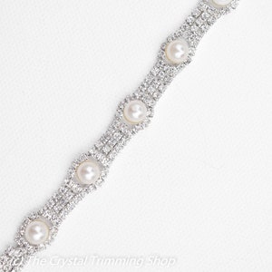 May include: A silver chain with clear rhinestones and white pearl accents. The chain is designed in a repeating pattern of square shapes with a pearl in the center of each square.