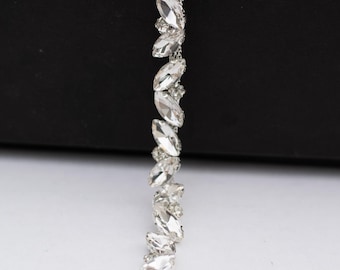 May include: A close-up of a silver-toned, decorative trim featuring clear, marquise-shaped rhinestones. The rhinestones are arranged in a vertical pattern, creating a sparkling, elegant design. The trim is set against a black background.