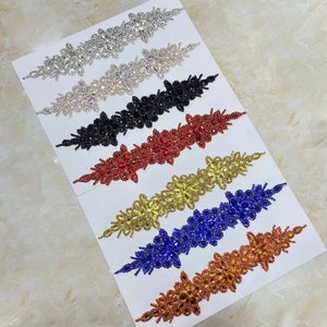 May include: Assortment of seven rhinestone embellishments in various colors, including silver, clear, black, red, gold, blue, and copper. Each embellishment features a floral design with multiple layers of rhinestones.