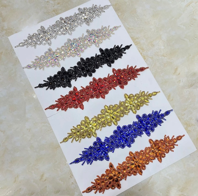 May include: Assortment of seven rhinestone embellishments in various colors, including silver, clear, black, red, gold, blue, and copper. Each embellishment features a floral design with multiple layers of rhinestones.
