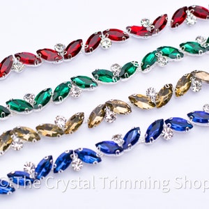 May include: A close-up of four rows of silver chain trim with marquise-shaped crystals. The crystals are in shades of red, green, gold, and blue.