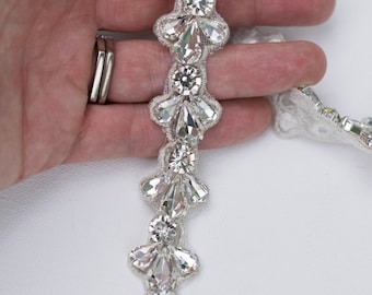 May include: A silver beaded trim with clear teardrop-shaped crystals. The trim is on a white background.